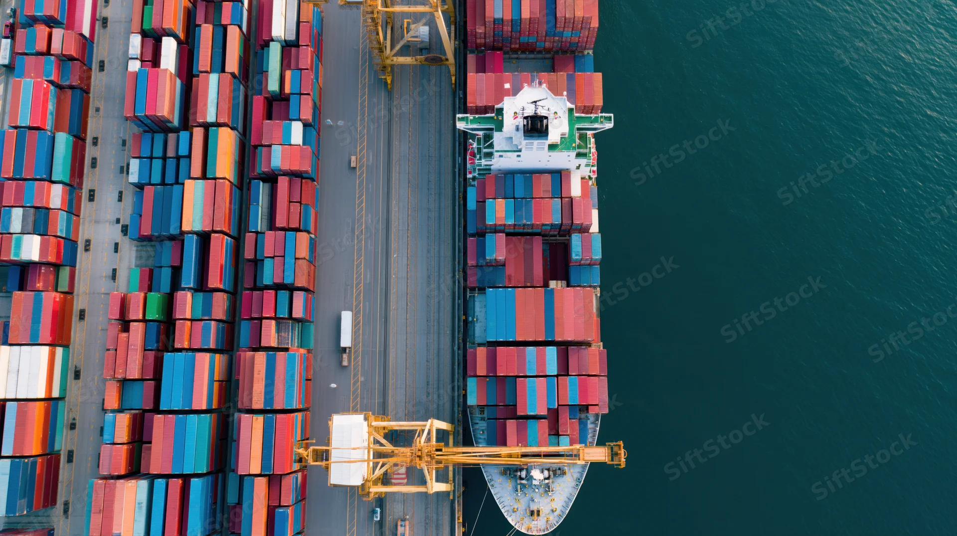 Aerial top-down view of a container ship docked at a port with stacked cargo containers and cranes nearby