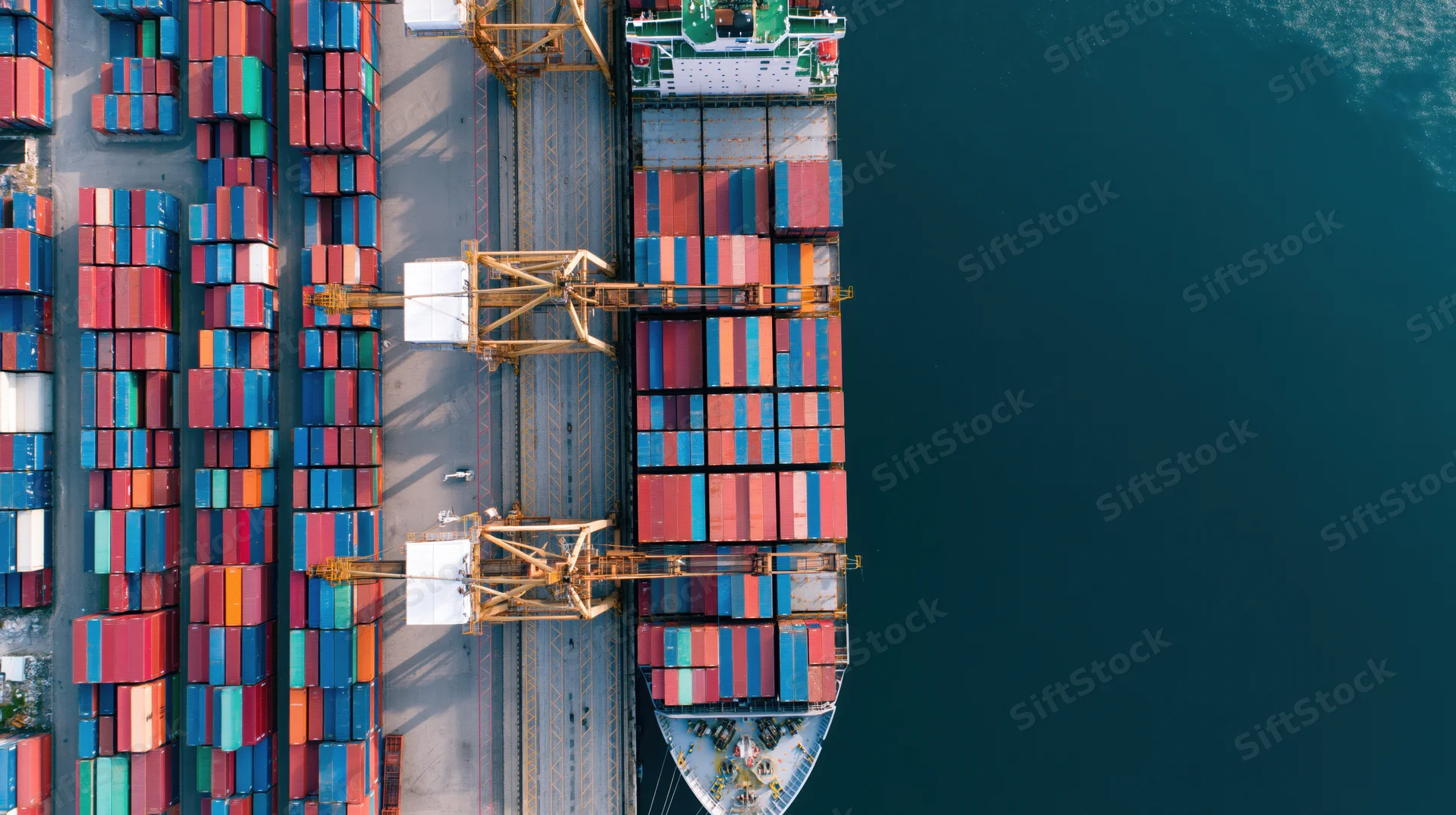 Aerial top-down view of a container ship docked at a port with cranes loading cargo containers