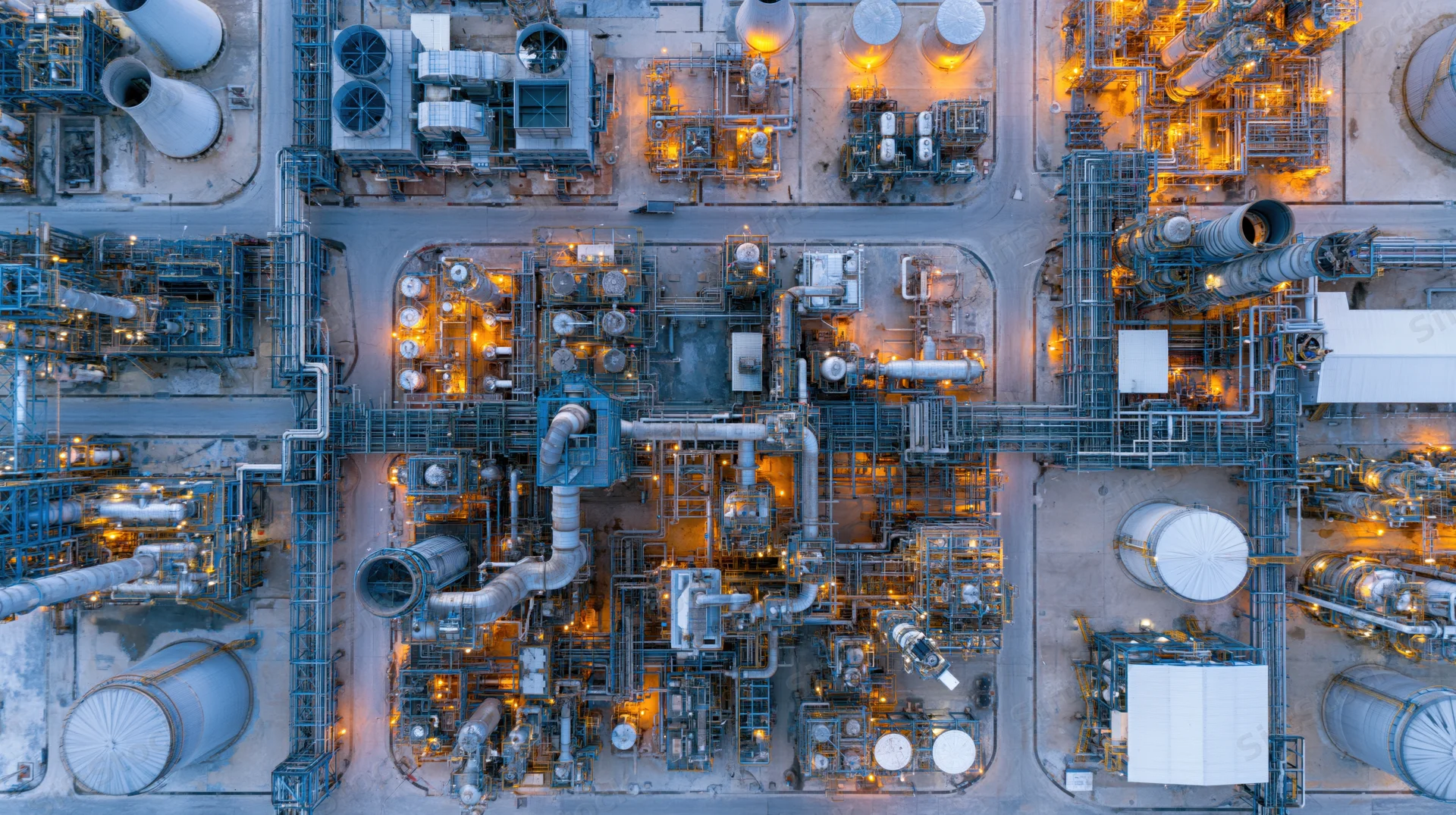 Aerial top-down view of a large petrochemical refinery at night with illuminated pipes and storage tanks
