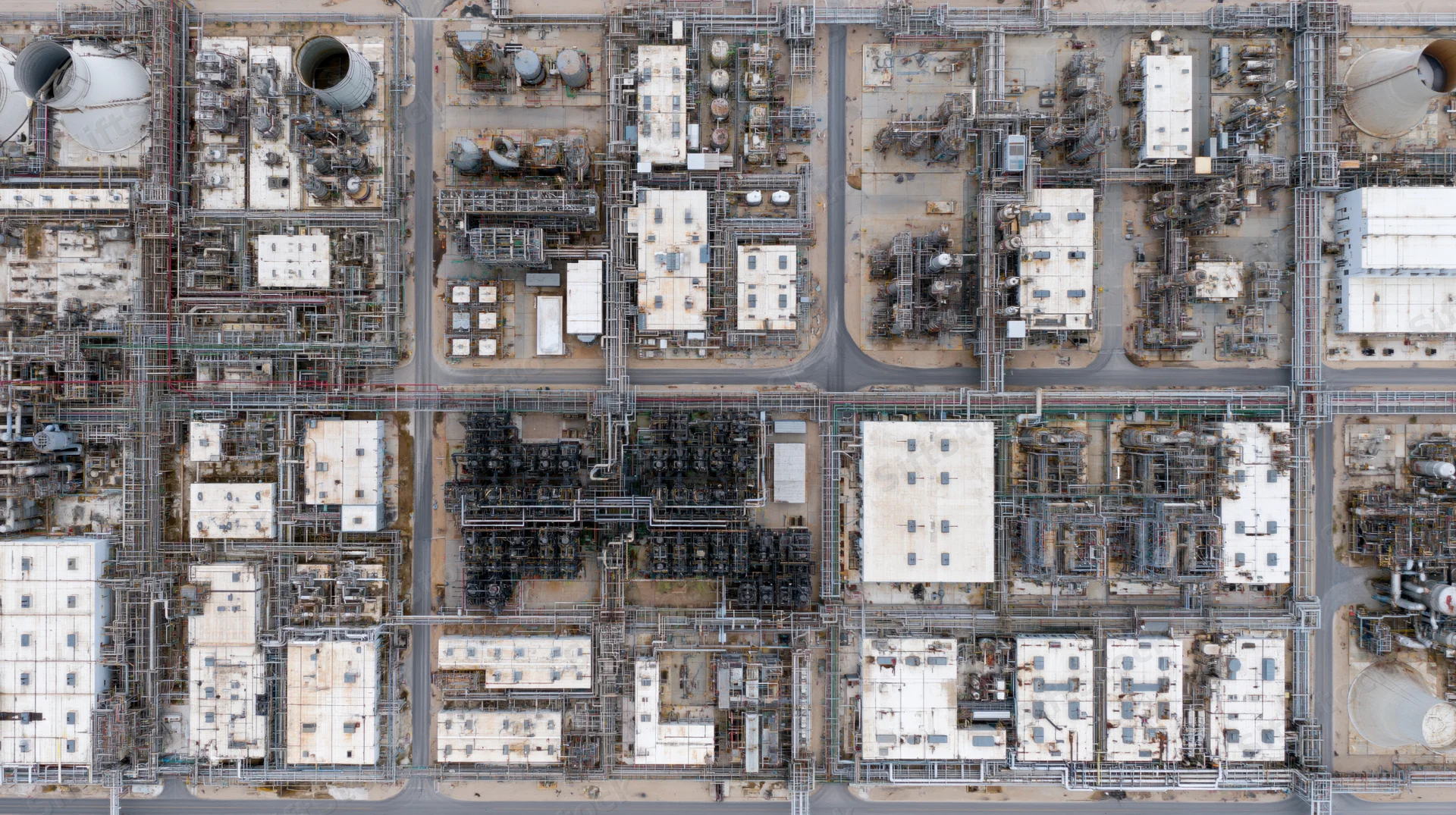 Aerial top-down view of a large petrochemical plant with interconnected tanks, pipes, and buildings