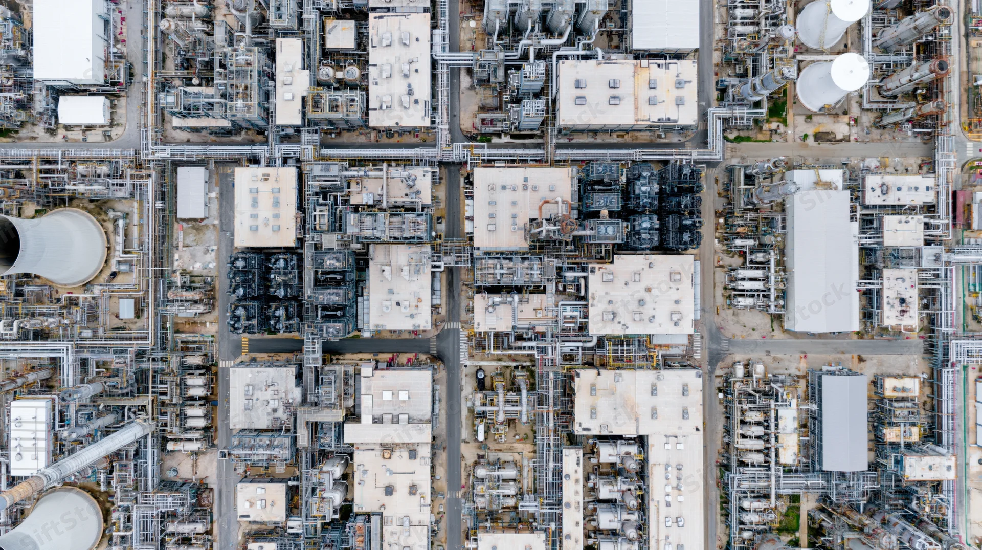 Aerial top-down view of a large petrochemical plant with interconnected towers, tanks, and pipelines