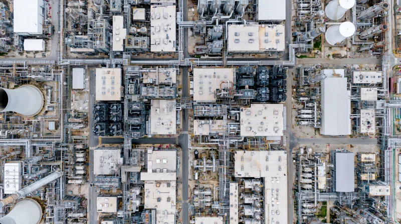 Aerial top-down view of a large petrochemical plant with interconnected towers, tanks, and pipelines
