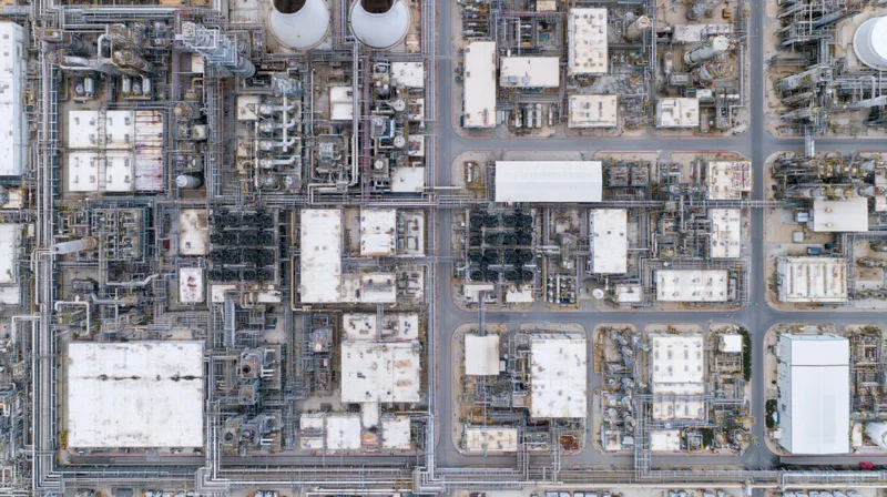 Aerial top-down view of a large petrochemical plant with interconnected pipes, storage tanks, and processing units arranged in a grid pattern across an industrial complex