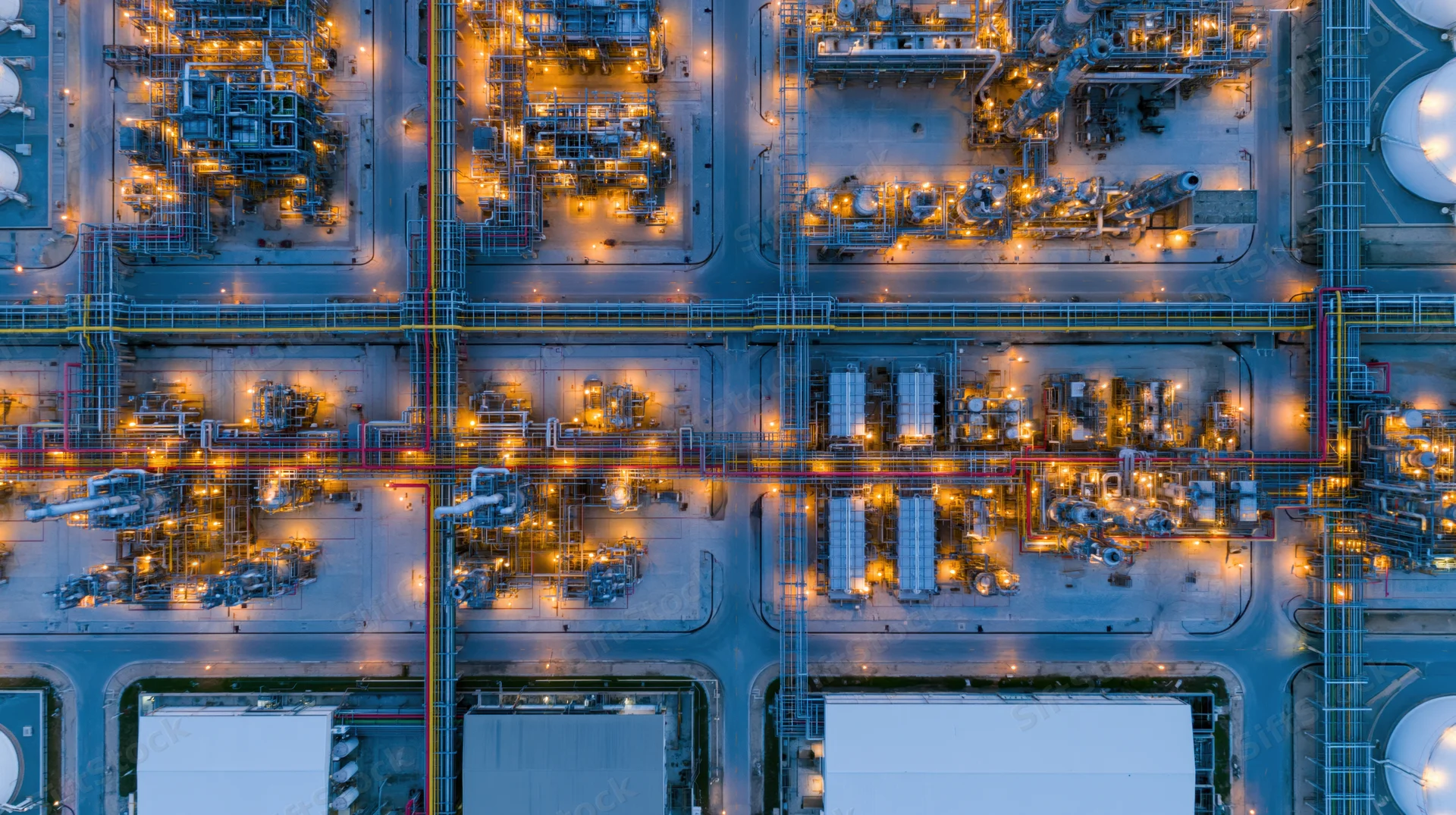 Aerial top-down view of a large industrial petrochemical plant at night with illuminated machinery and pipelines
