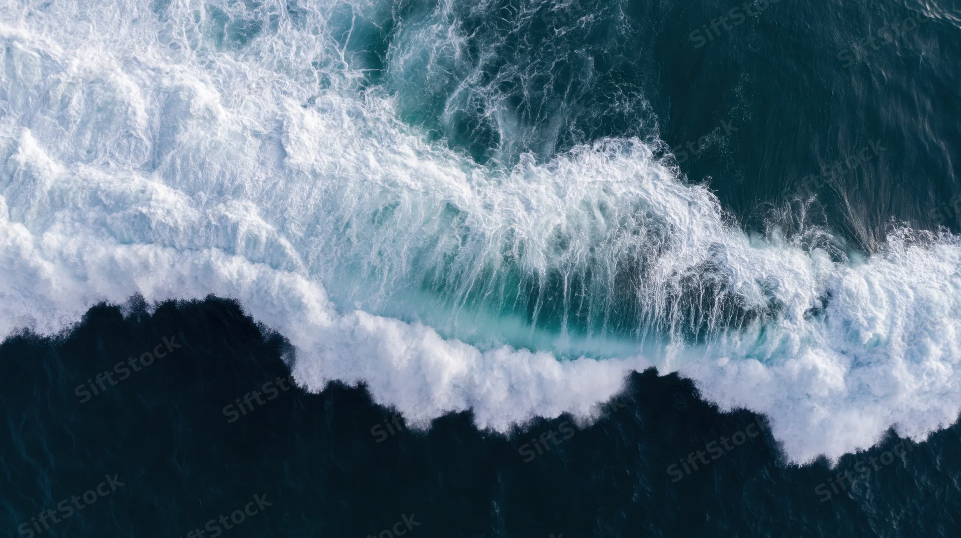 Aerial top-down view of a large ocean wave breaking with white foam and deep blue water