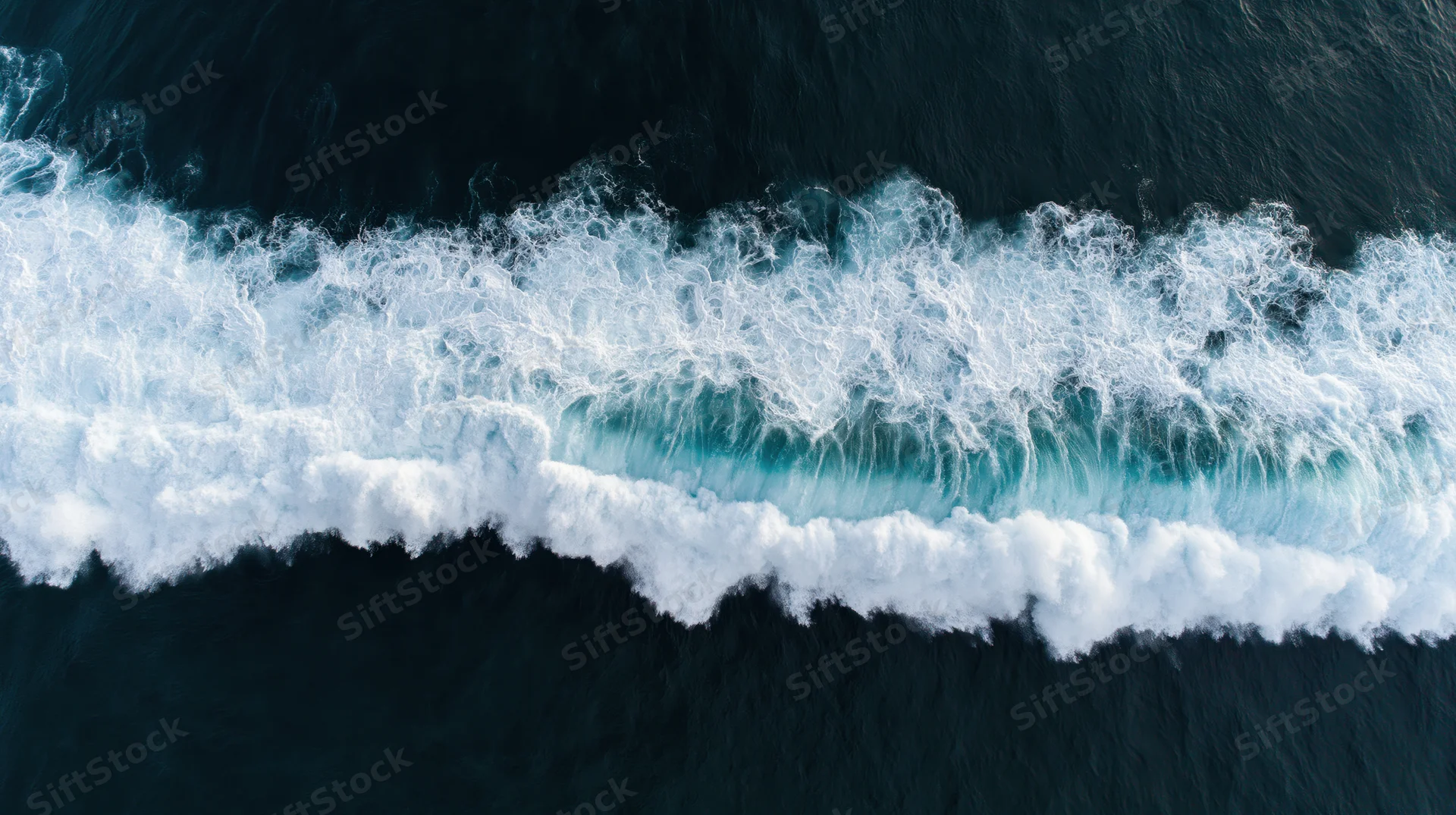 Aerial top-down view of a large ocean wave breaking with white foam and deep blue water