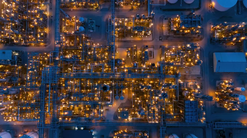 Aerial top-down view of a large oil refinery and petrochemical plant at night with illuminated structures and pipelines