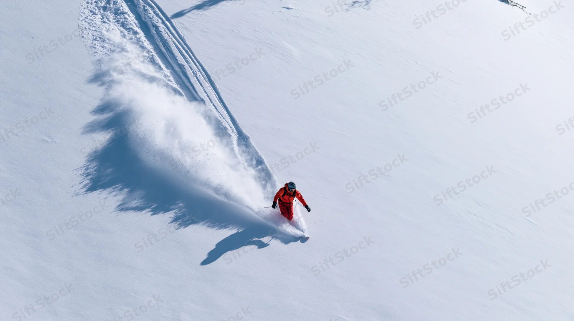 Skier carving through deep powder snow on a mountain slope from an aerial view