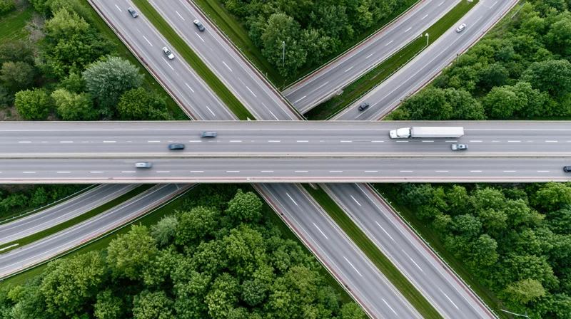 Aerial top-down view of a multi-level highway interchange with vehicles moving across overpasses surrounded by green trees