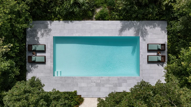 Aerial top-down view of a rectangular outdoor swimming pool surrounded by green trees and stone deck with lounge chairs