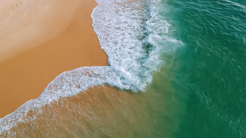 Aerial top-down view of waves breaking on a sandy beach shoreline
