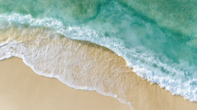 Aerial top-down view of turquoise ocean waves meeting sandy beach