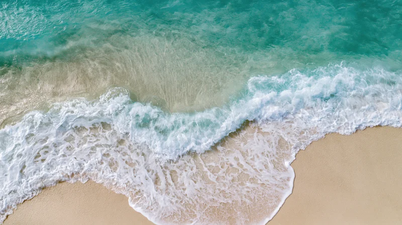 Aerial top-down view of turquoise ocean waves breaking on sandy tropical shoreline