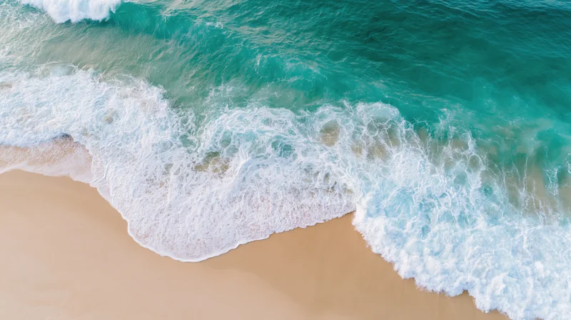 Aerial top-down view of turquoise ocean waves crashing onto sandy beach