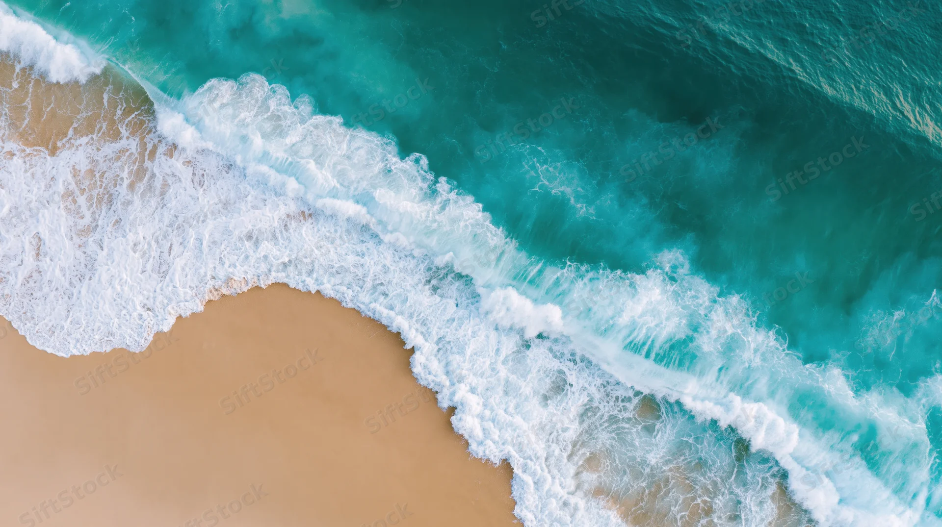 Aerial top-down view of turquoise ocean waves crashing onto sandy shoreline