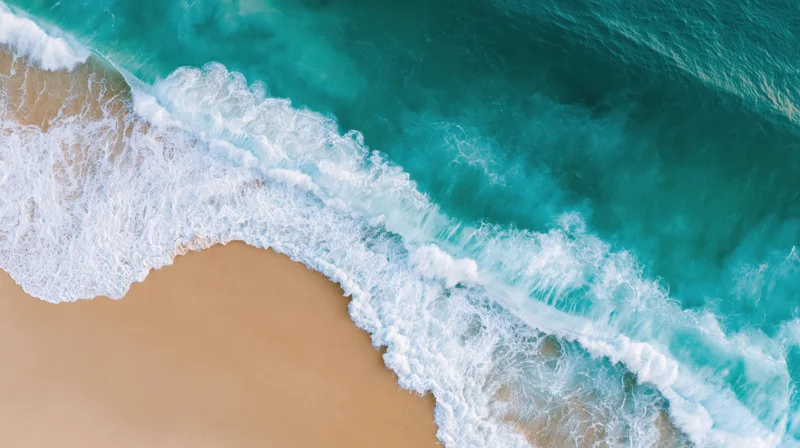 Aerial top-down view of turquoise ocean waves crashing onto sandy shoreline