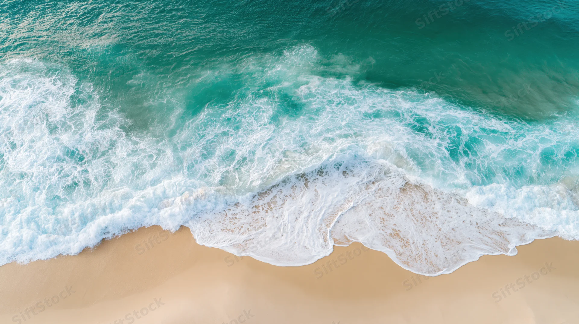 Aerial top-down view of turquoise ocean waves breaking on sandy beach