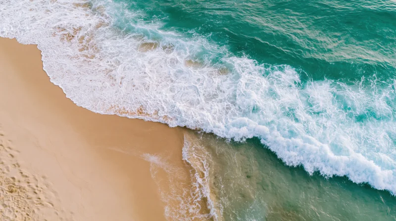 Aerial top-down view of turquoise ocean waves breaking on sandy shoreline