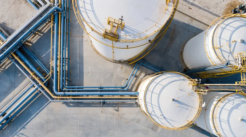Aerial top-down view of industrial gas storage facility with white tanks and blue pipelines on concrete ground