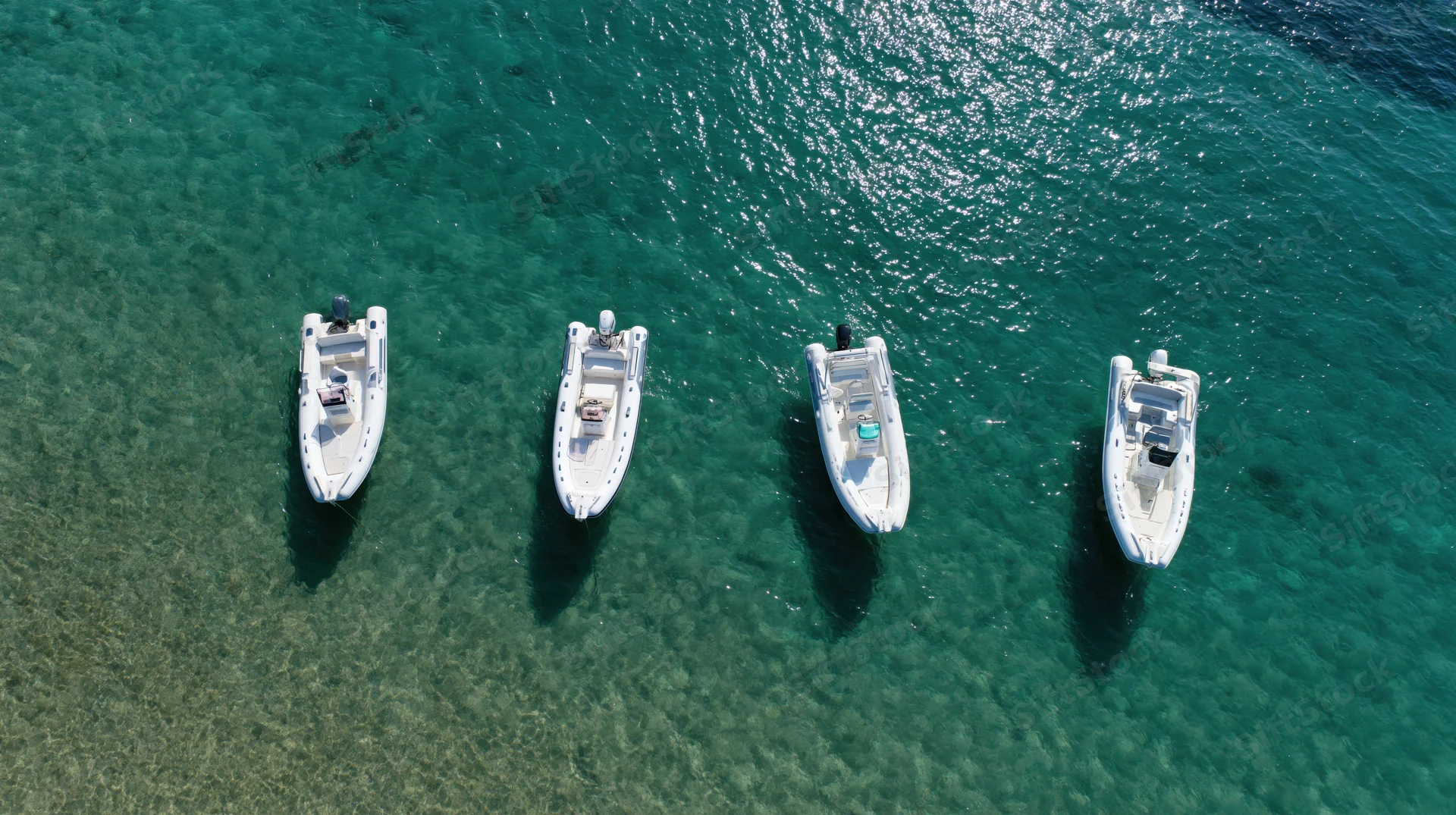 Four small motorboats anchored in clear turquoise water viewed from above