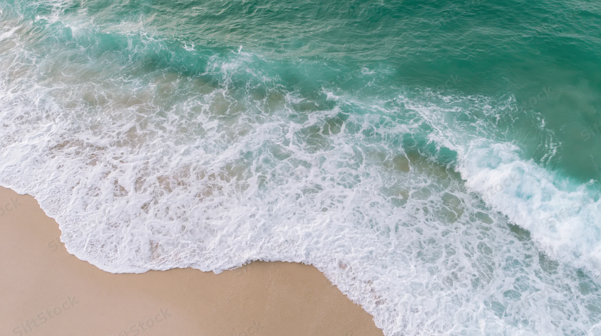Aerial top-down view of gentle ocean waves washing onto a sandy beach