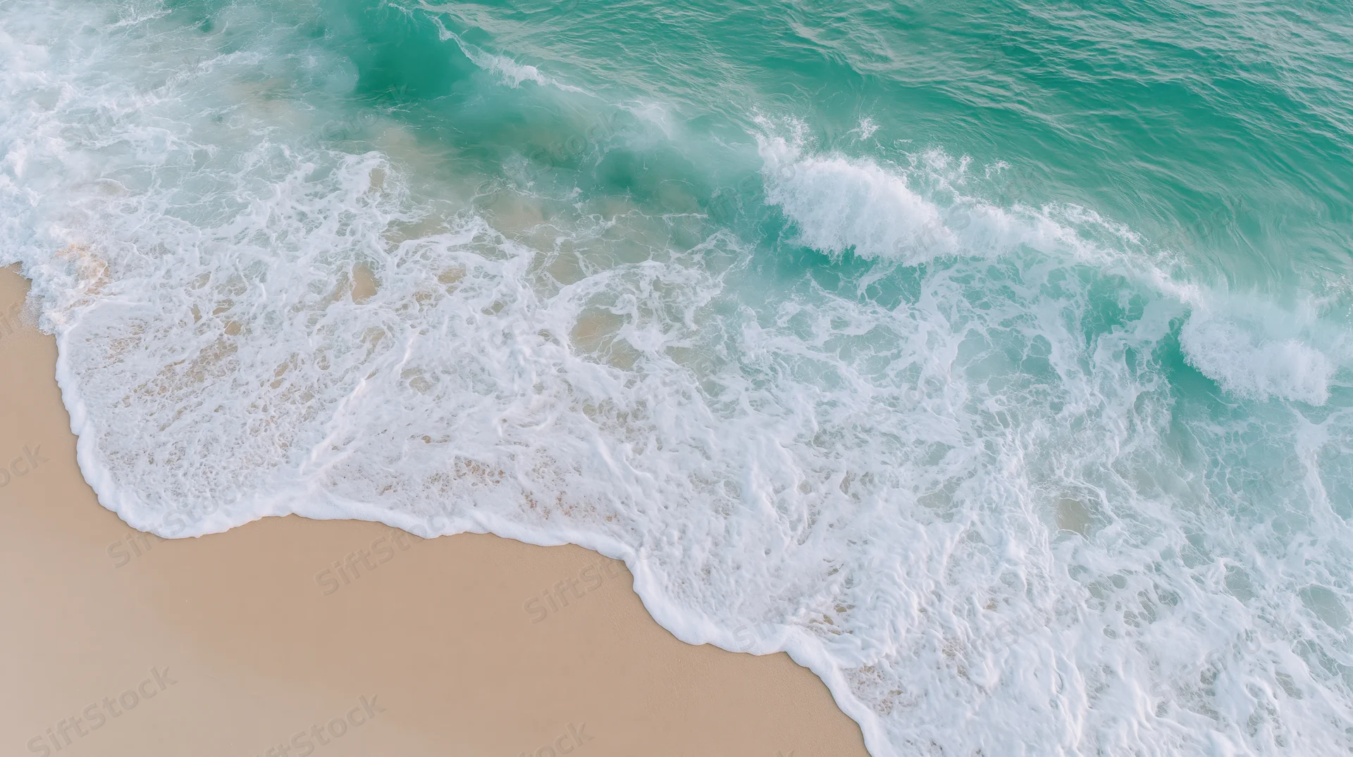 Aerial top-down view of gentle ocean waves washing onto a sandy beach
