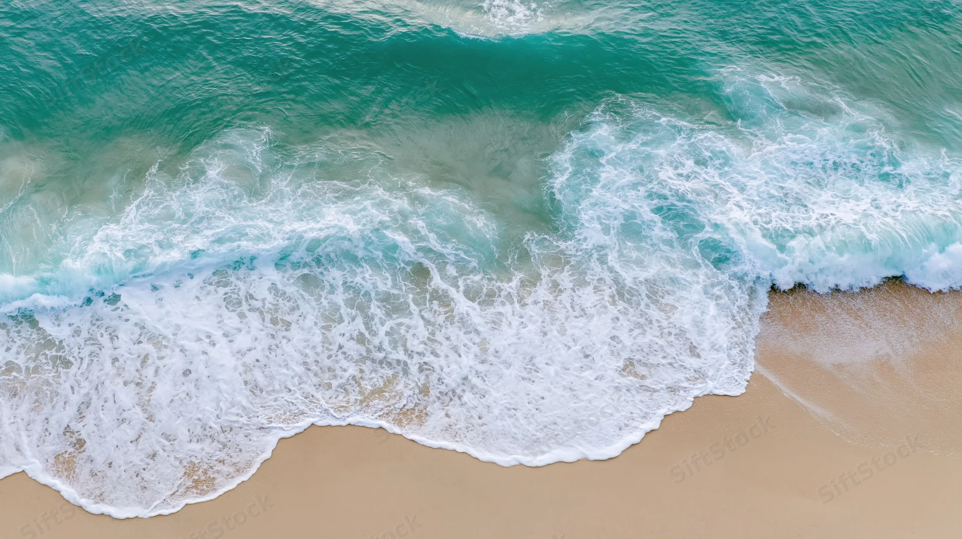 Aerial top-down view of gentle ocean waves washing onto a sandy beach