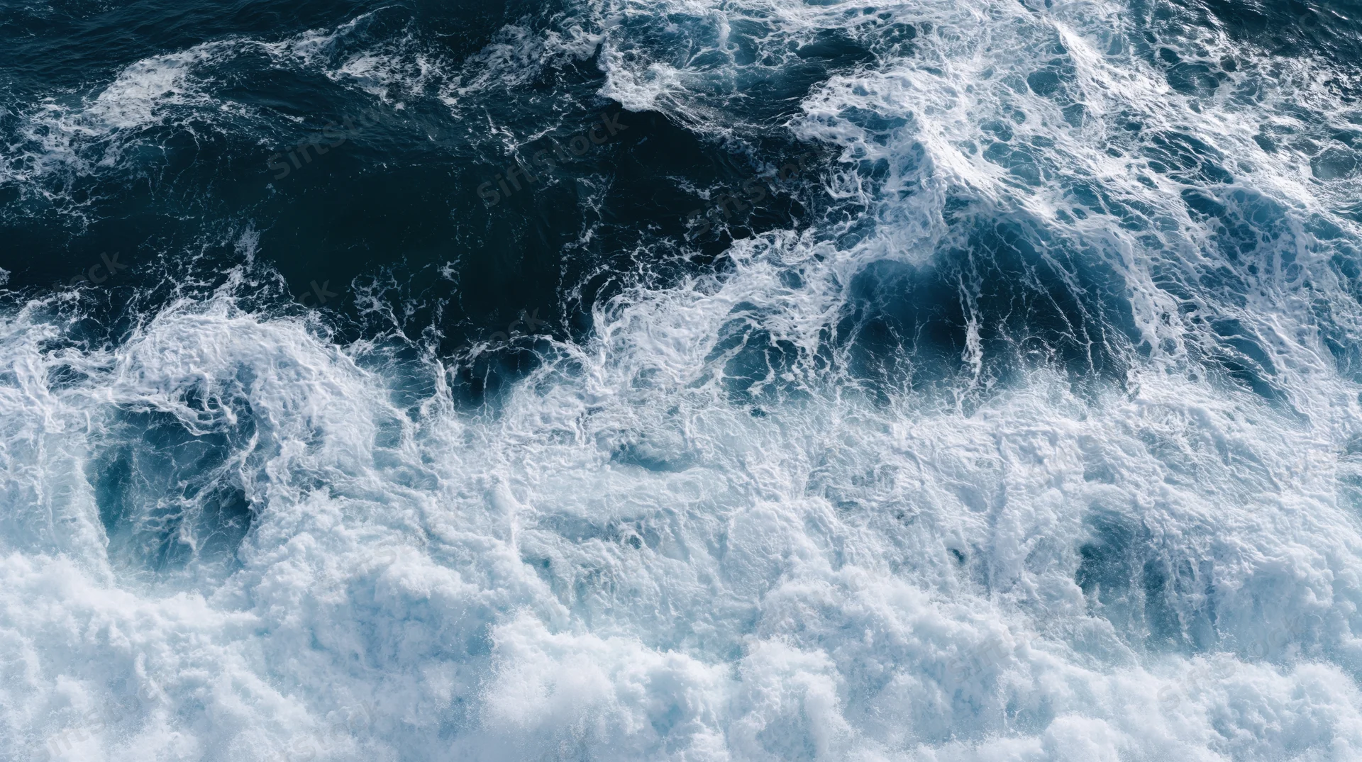 Aerial top-down view of ocean waves breaking and churning with white foam on dark blue water surface