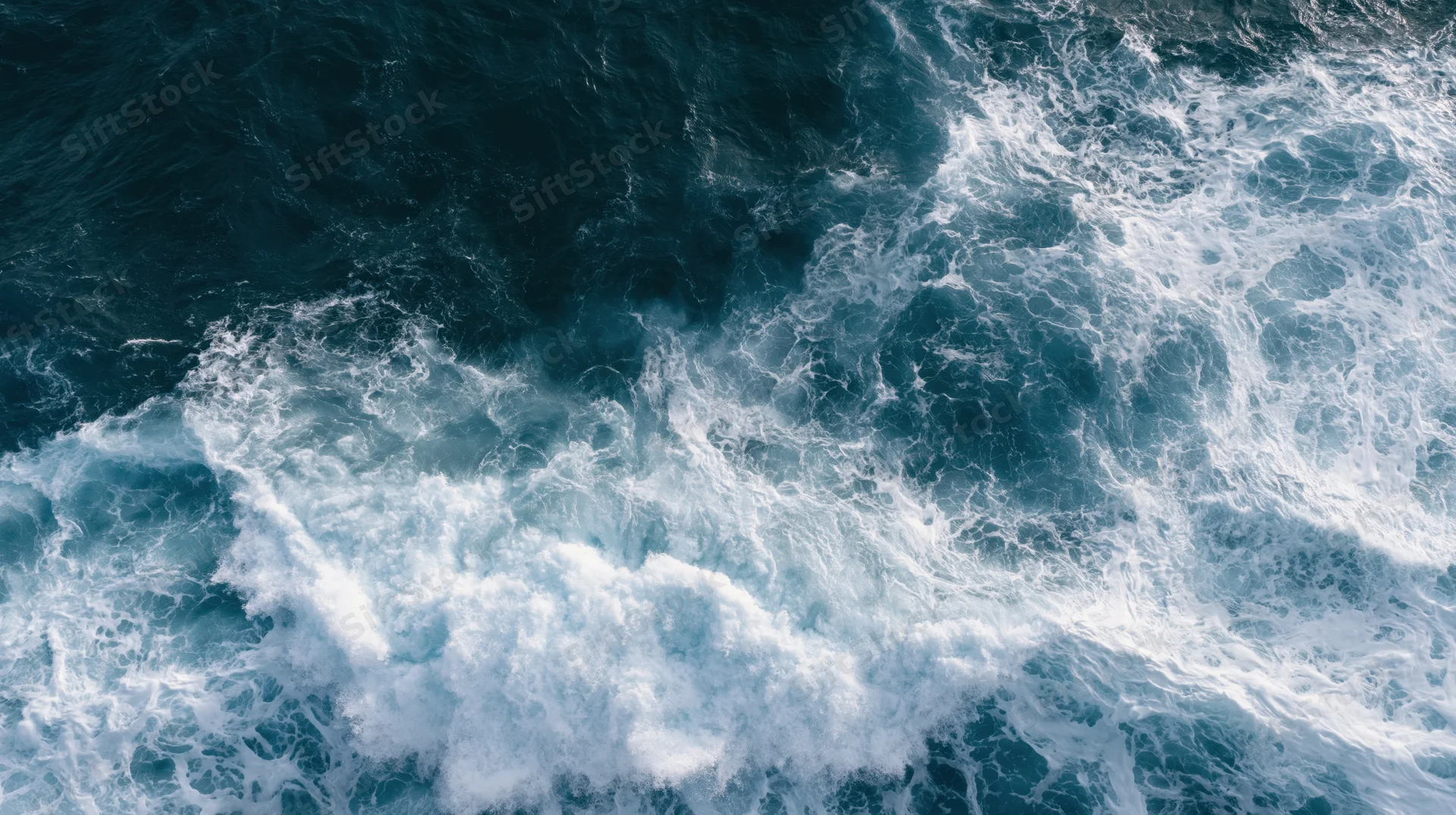 Aerial top-down view of ocean waves breaking and churning with white foam on dark blue water