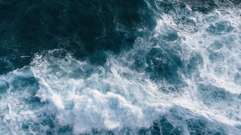 Aerial top-down view of ocean waves breaking and churning with white foam on dark blue water