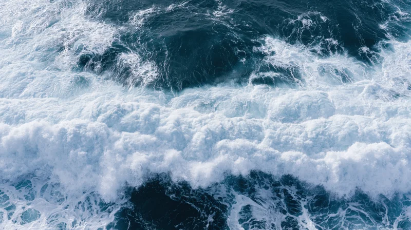 Aerial top-down view of ocean waves breaking and churning with white foam on deep blue water