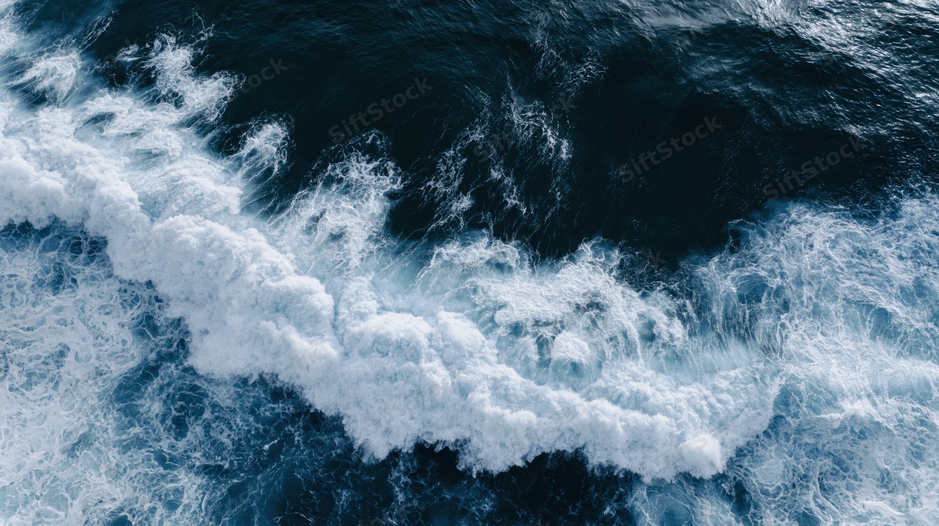 Aerial top-down view of ocean waves breaking and churning with white foam on dark blue water