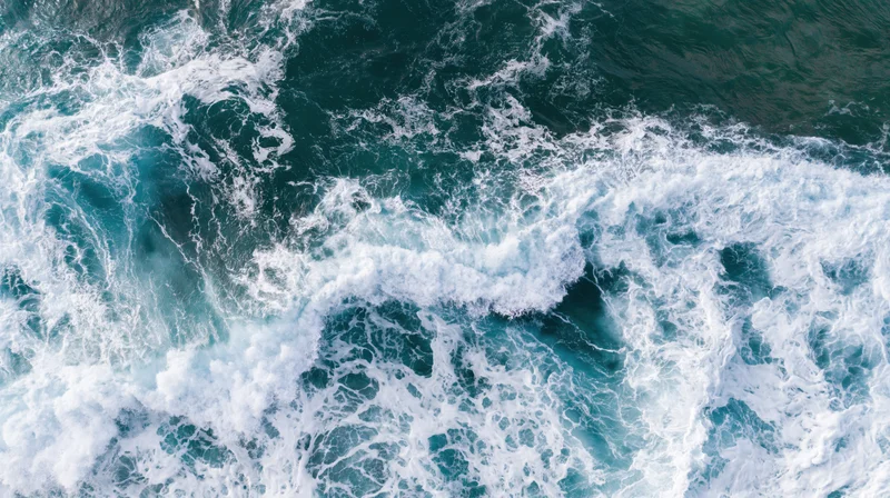 Aerial top-down view of ocean waves breaking and churning with white foam on blue water surface