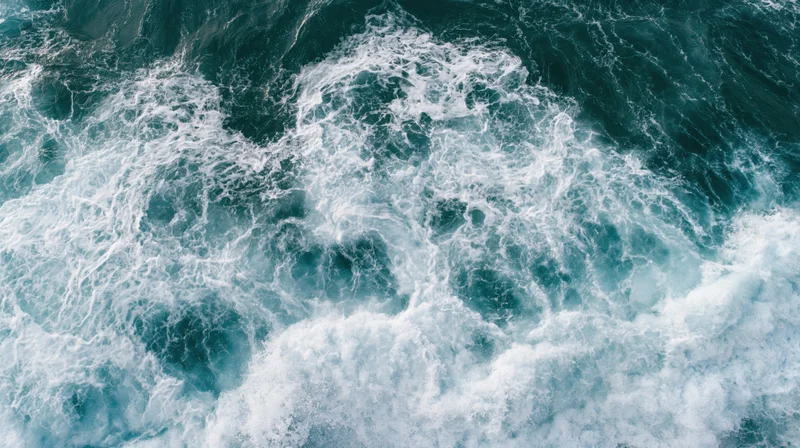 Aerial top-down view of ocean waves breaking and churning with white foam on blue water surface