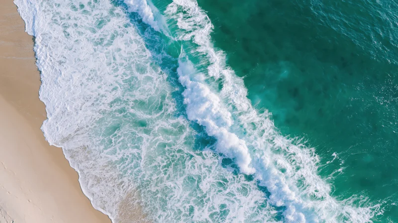 Aerial top-down view of ocean waves breaking onto pale sand