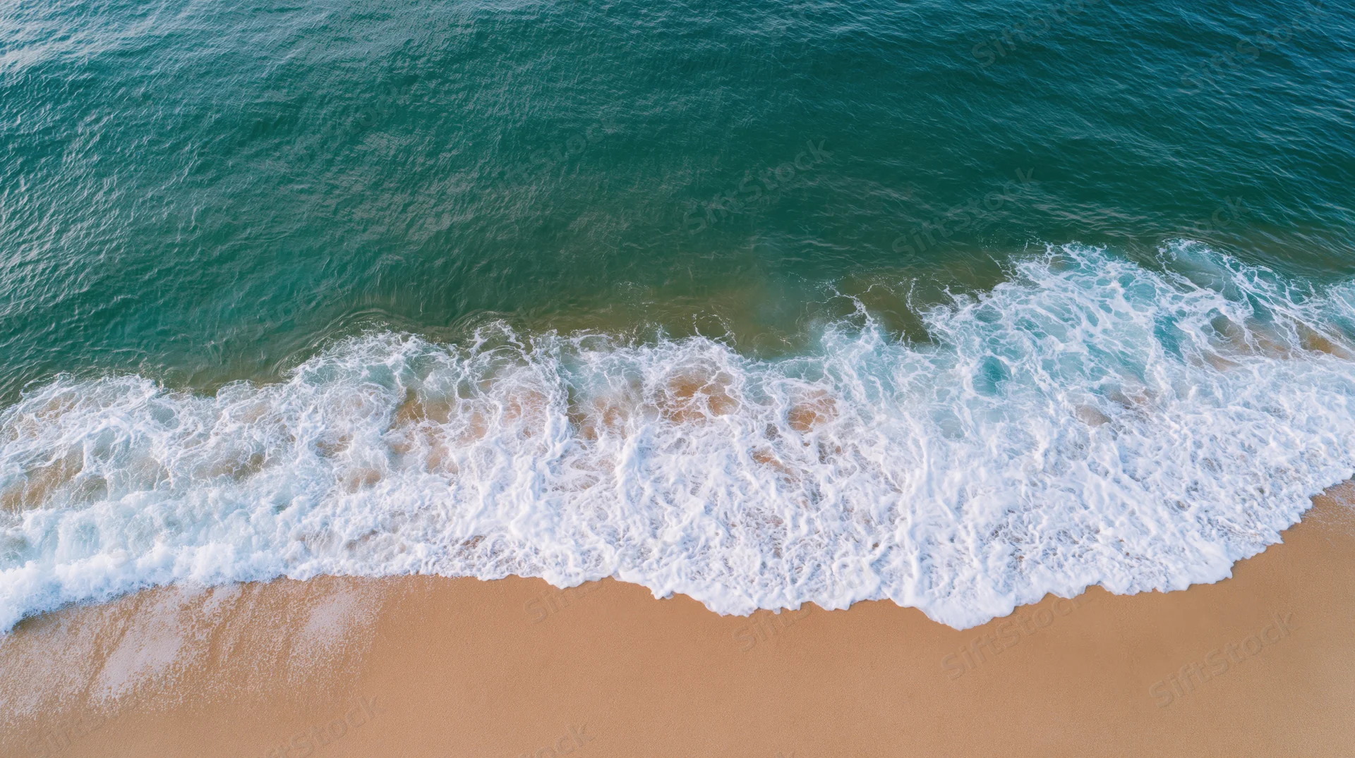 Aerial top-down view of ocean waves breaking onto a sandy beach