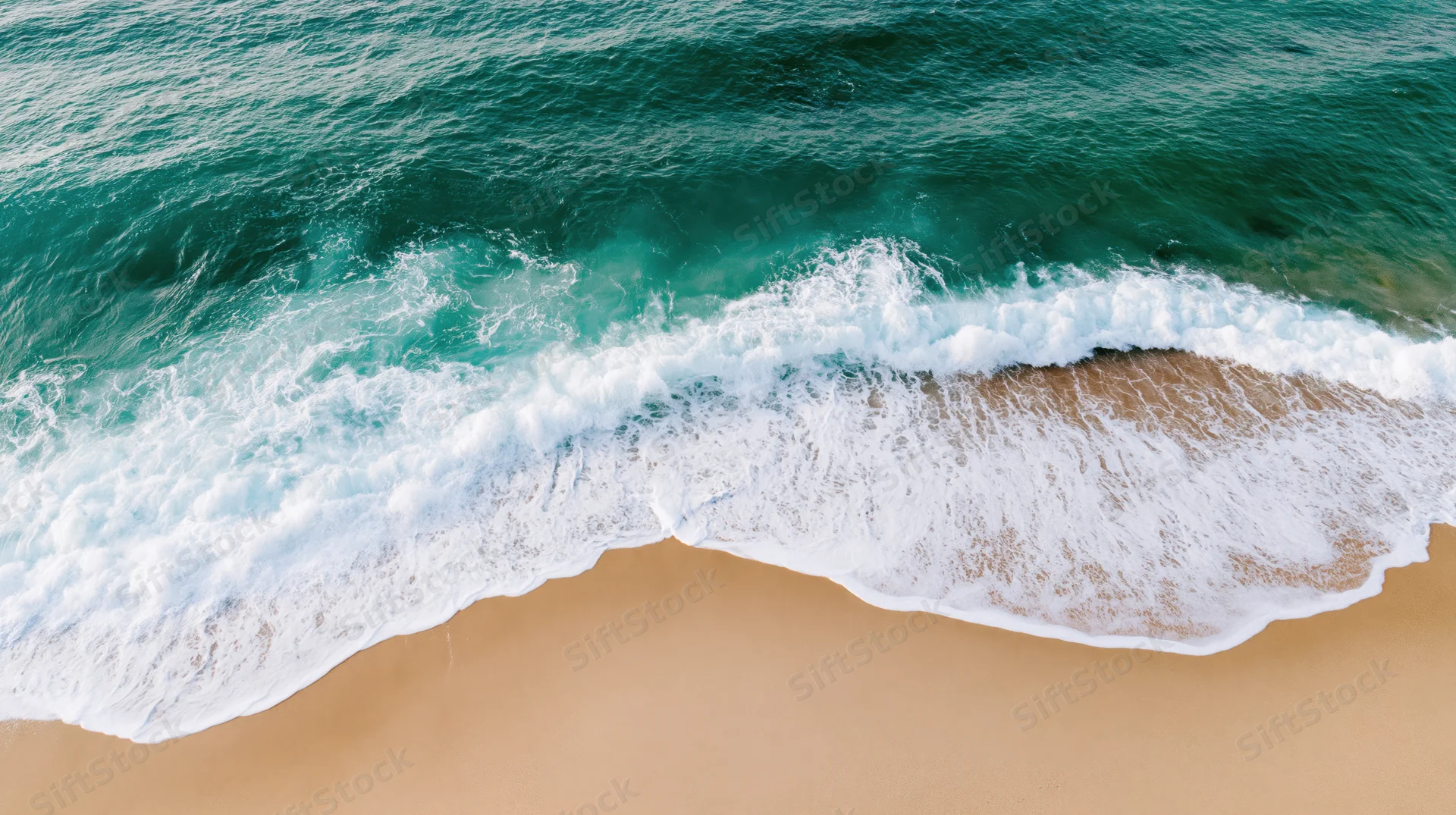 Aerial top-down view of ocean waves breaking onto sandy beach
