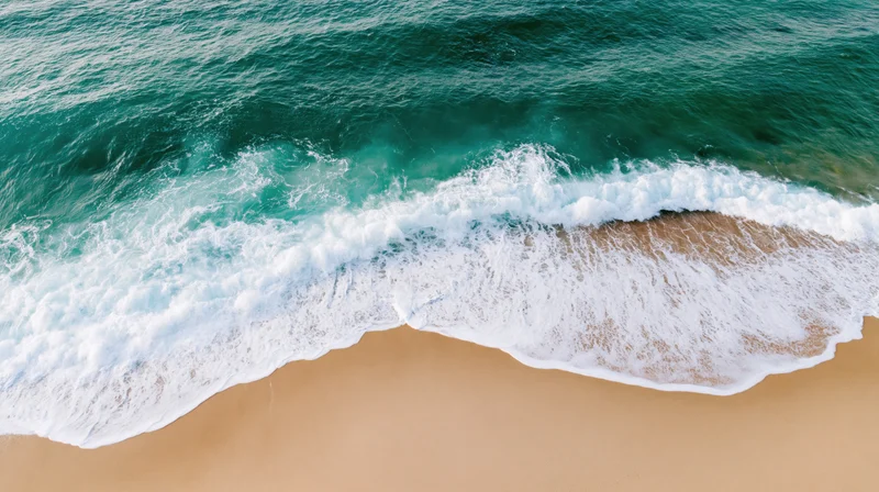 Aerial top-down view of ocean waves breaking onto sandy beach