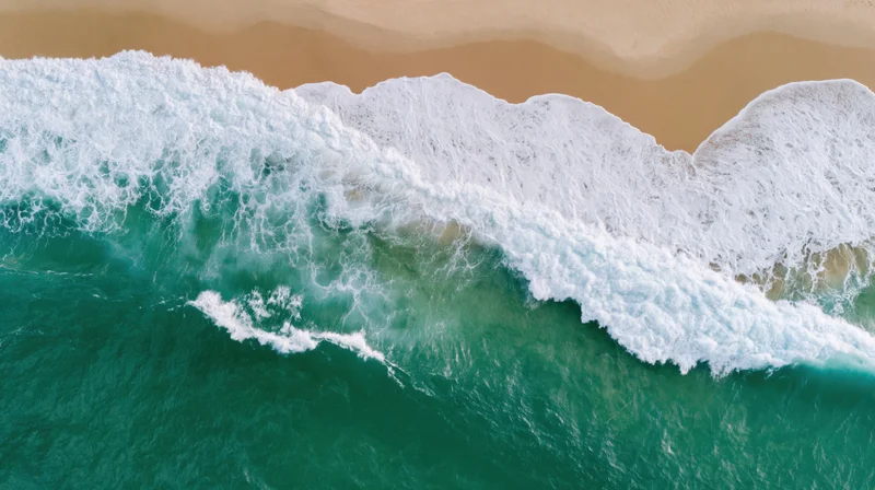 Aerial top-down view of ocean waves breaking onto sandy beach