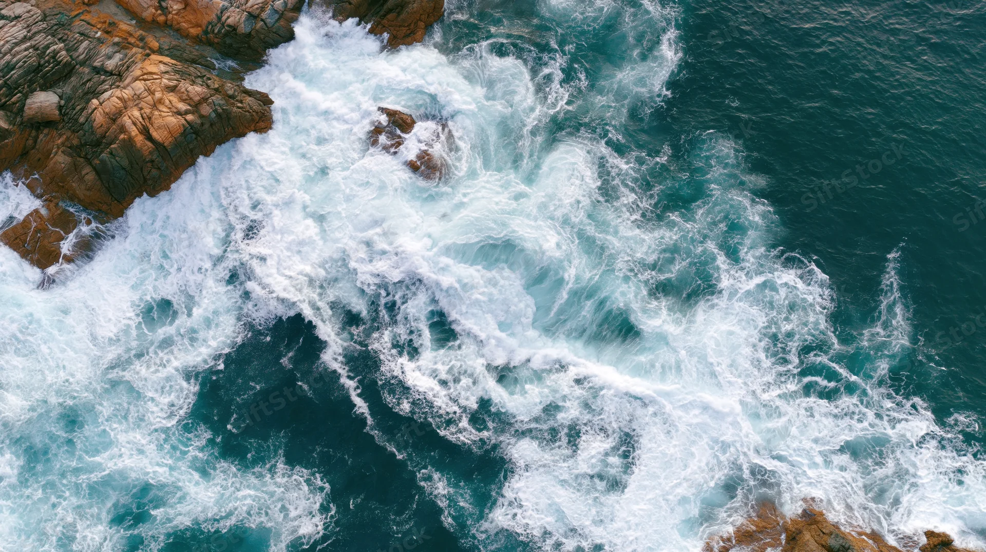 Aerial top-down view of ocean waves crashing against rocky coastline