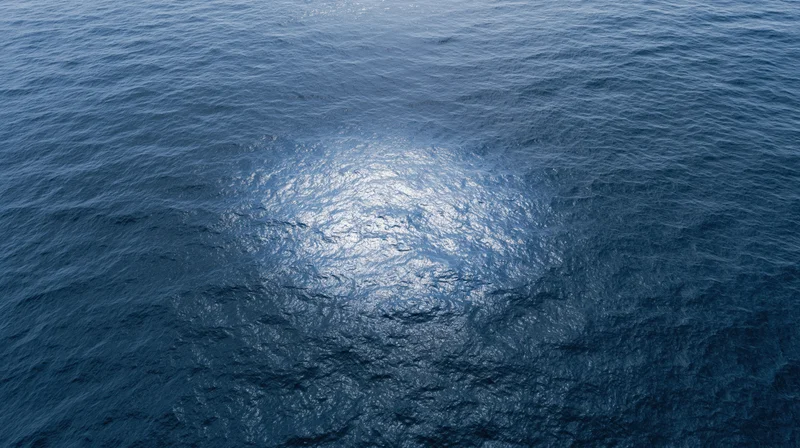 Aerial top-down view of open ocean surface with sunlight reflecting on rippling water