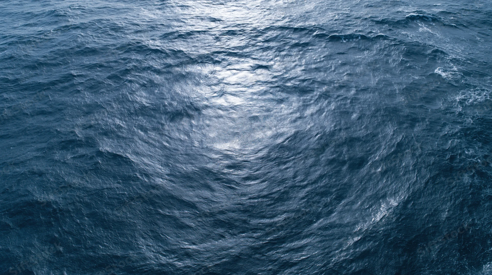 Aerial top-down view of open ocean surface with small waves and light reflections