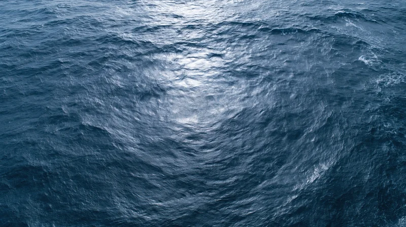 Aerial top-down view of open ocean surface with small waves and light reflections