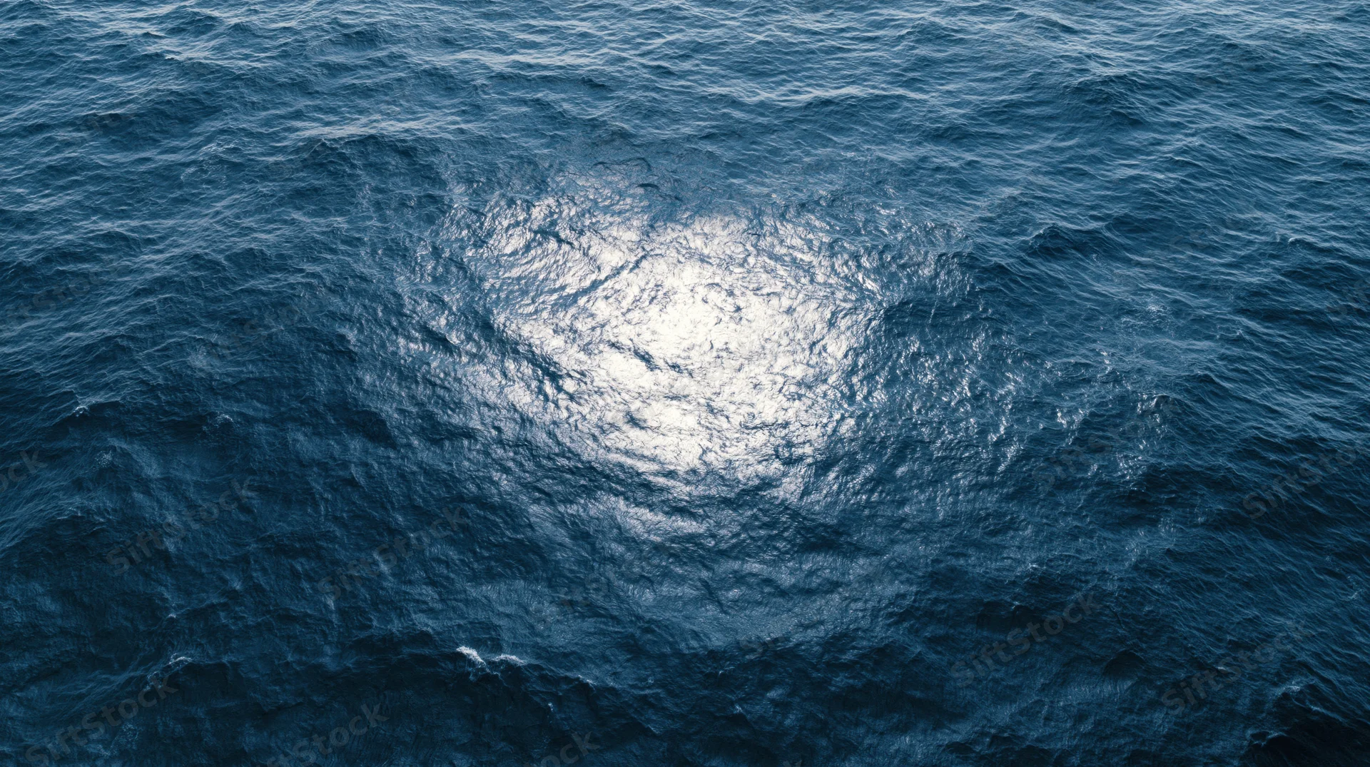 Aerial top-down view of open ocean surface with sunlight reflecting on rippling water