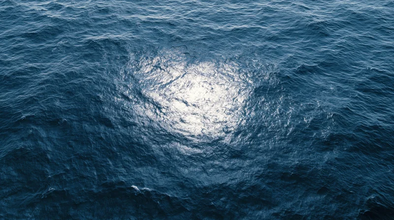 Aerial top-down view of open ocean surface with sunlight reflecting on rippling water
