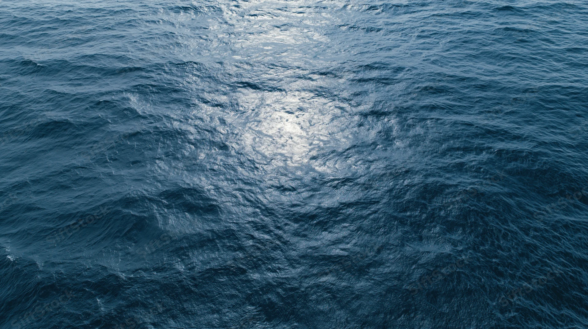 Aerial top-down view of open ocean surface with small waves and sunlight reflection