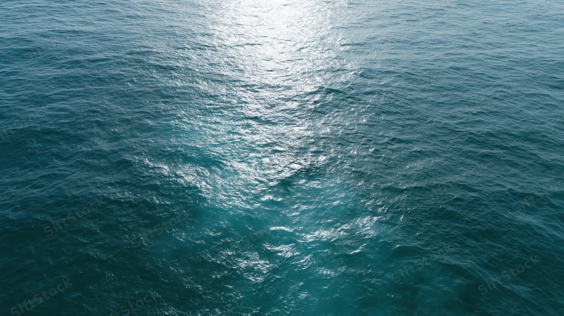 Aerial top-down view of open ocean surface with sunlight reflecting on rippling water