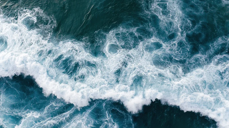 Aerial top-down view of turbulent ocean waves breaking and churning with white foam