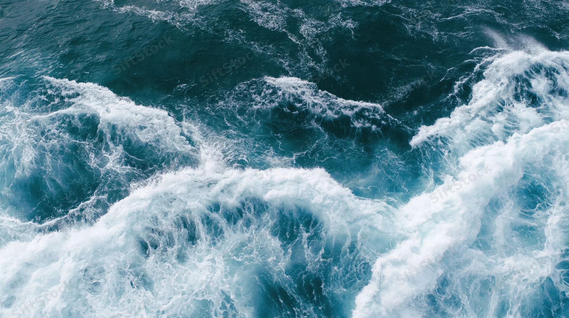 Aerial top-down view of turbulent ocean waves breaking and churning with white foam