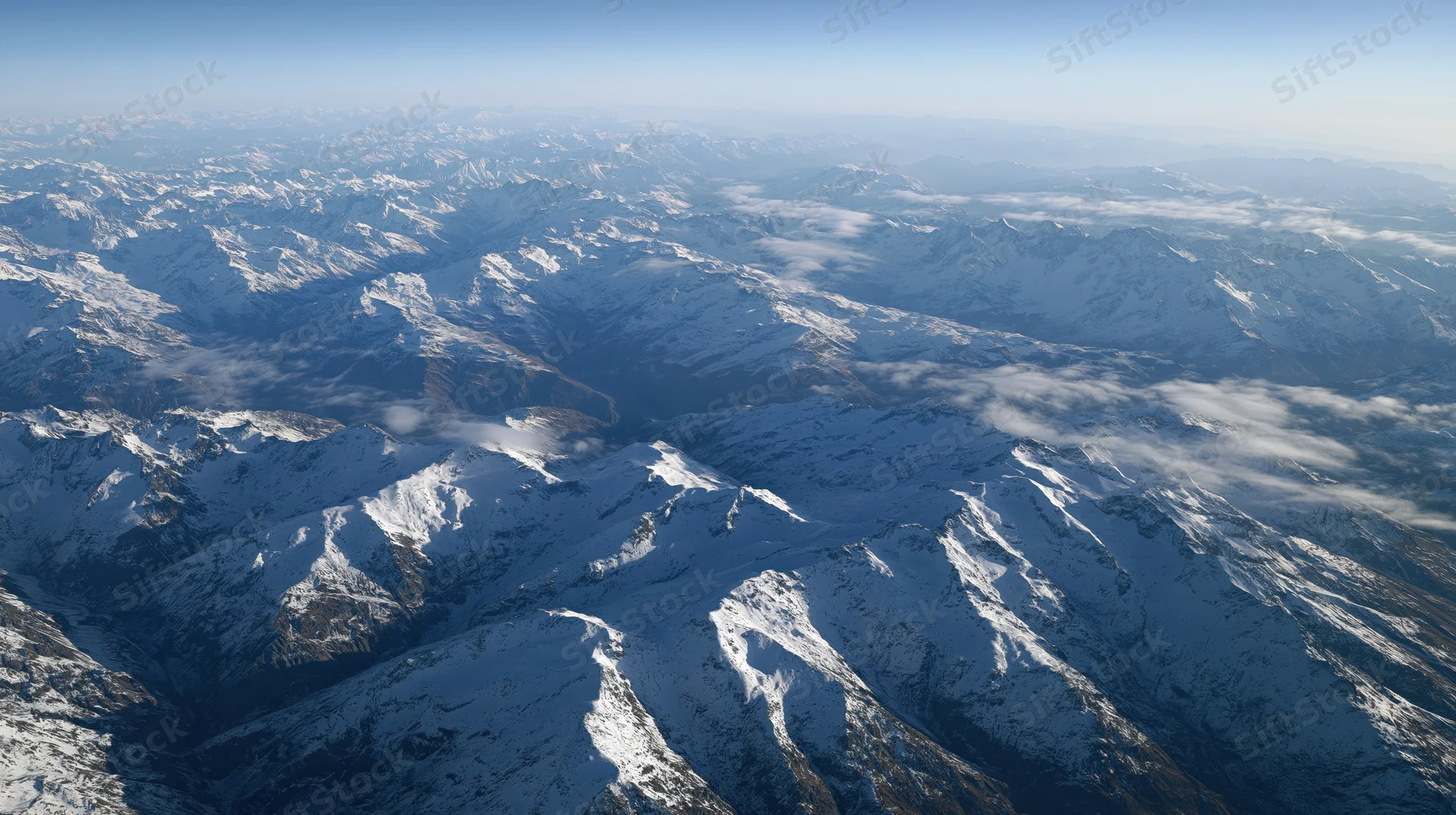 Aerial view of snow-covered mountain range with peaks and valleys under clear sky